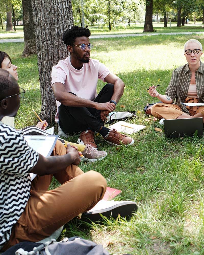 Une équipe fait une réunion assis par terre au milieu d'une forêt