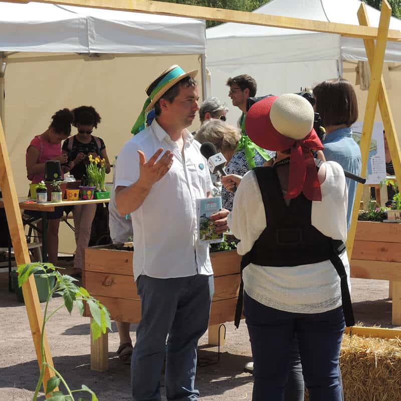 Un homme et une femme discutent au milieu d'un événement extérieur avec des stands d'exposition derrière eux