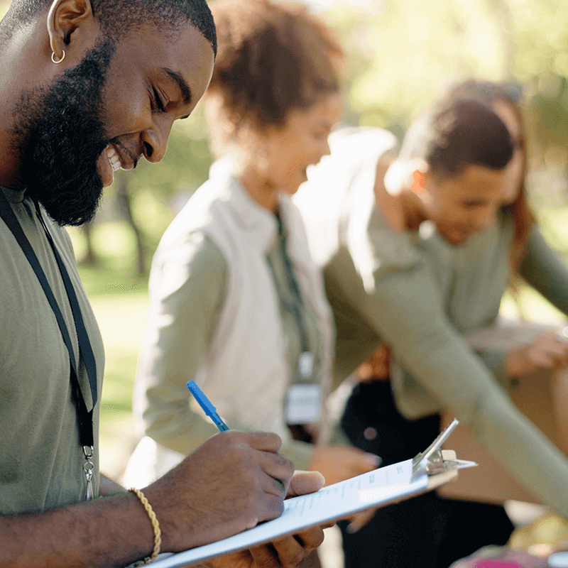 illustration-chantier-d-application Un homme sourit au premier plan en prenant des notes devant d'autres personnes souriantes dans une forêt