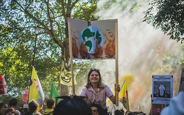Foule de manifestant avec une femme sur les épaules de quelques portant une pancarte avec une planète en feu